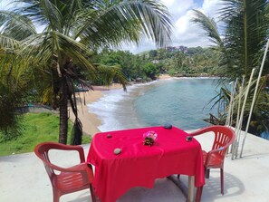 A table with a red tablecloth, two chairs, and a decorative centerpiece on a balcony overlooking a beach with palm trees and a clear sky. - Surf Paradise Hotel  (Tangalle)