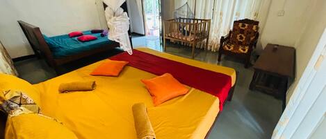 Une chambre avec deux lits, l’un recouvert d’une couvre-lit jaune et l’autre d’une couvre-lit verte. On y trouve une chaise avec un coussin à motifs et une petite table.