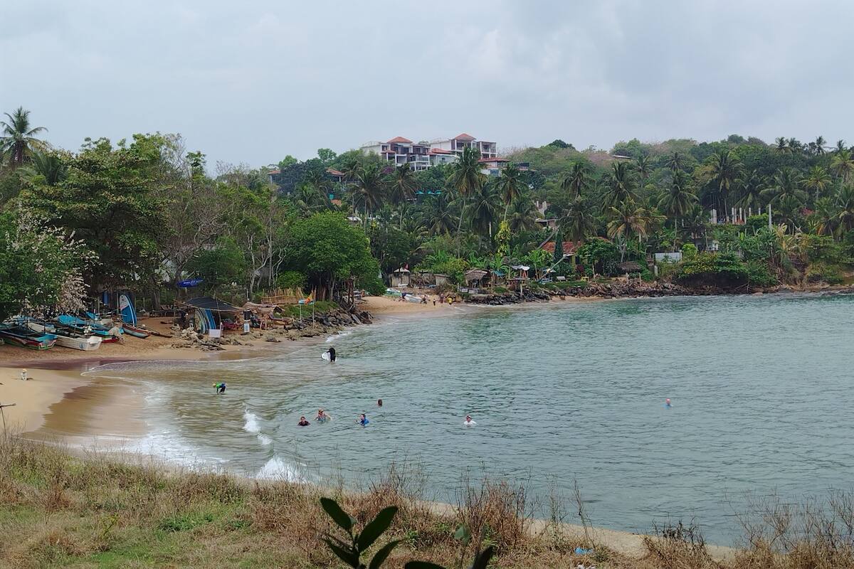 A beach with boats, people swimming, and a building in the background.