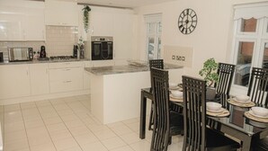 A modern kitchen with white cabinets, a built-in oven, and a dining area with a glass table and black chairs. - Lovely 3-Bed House in Solihull (Solihull)