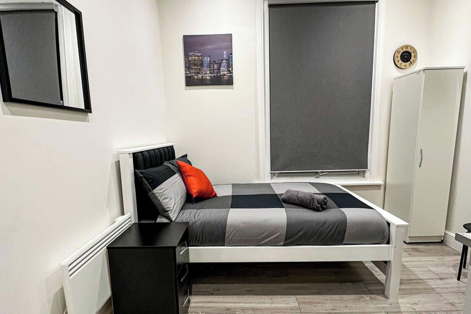 Un dormitorio con cama, ventana, armario y un cuadro en la pared.