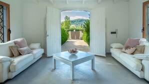 A room with two white sofas, a small table with a bowl, and a view of a garden through an open door. - Ca na Saurina by Interhome (Crestatx)