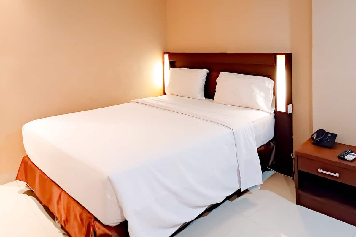 A neatly made bed with white linens in a hotel room.