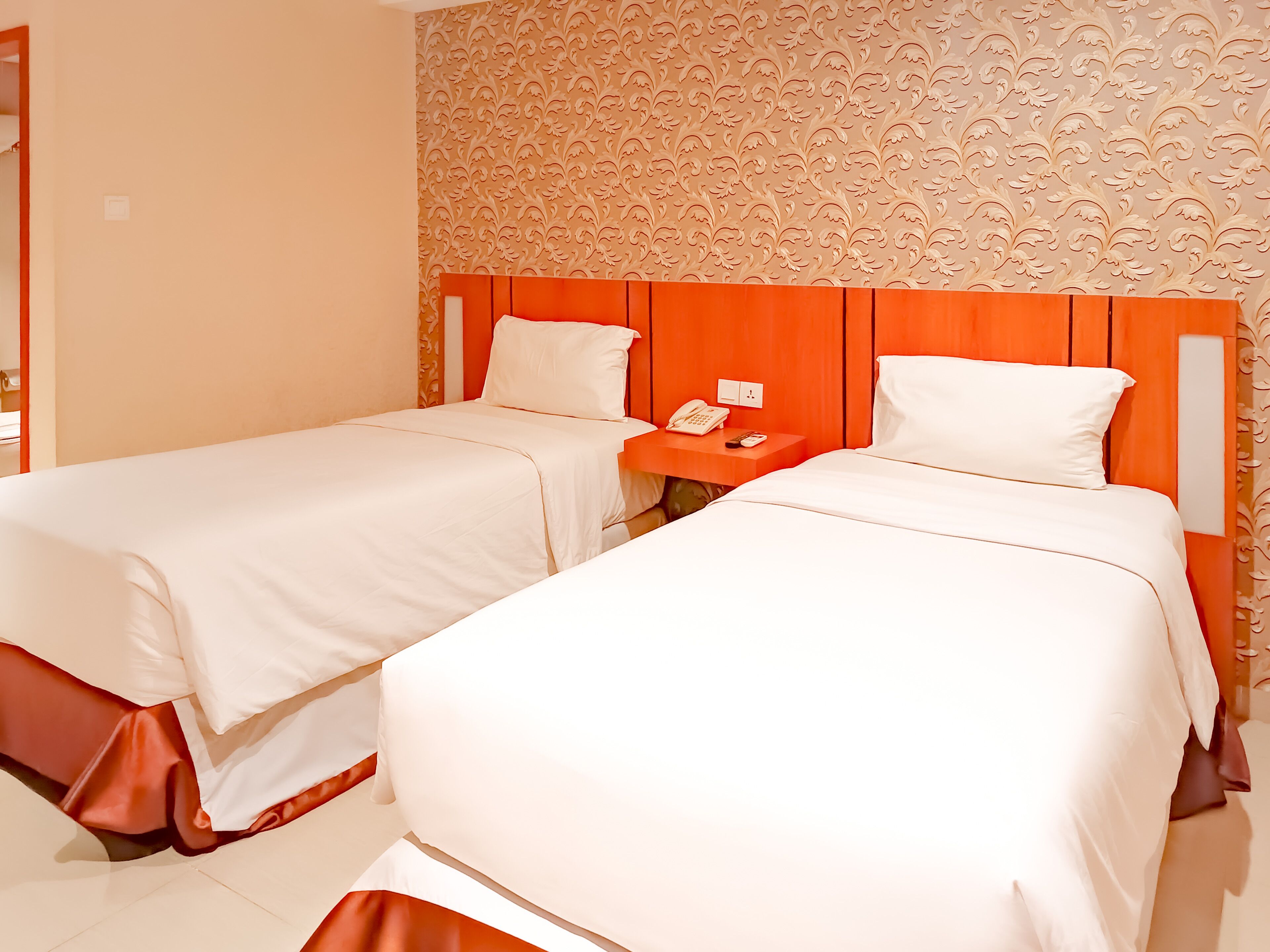 A hotel room with two beds, a nightstand, and a patterned wall.
