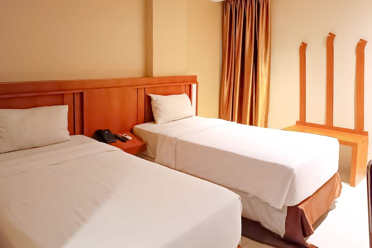 A hotel room with two beds, a wooden headboard, a nightstand with a phone and remote, and a window with curtains.