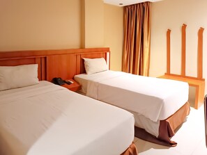 Habitación de hotel con dos camas, cabecera de madera, mesita de noche con teléfono y control remoto, y ventana con cortinas.