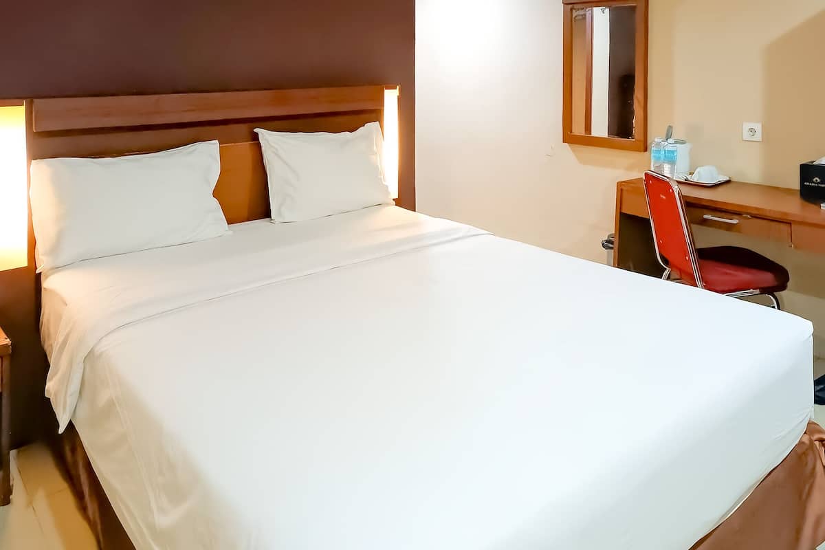 A neatly made bed with white linens, a wooden headboard, and a bedside table with a red chair.