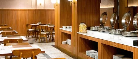 En restaurant med træpaneler, borde med stole og et buffetområde med tallerkener og skåle.