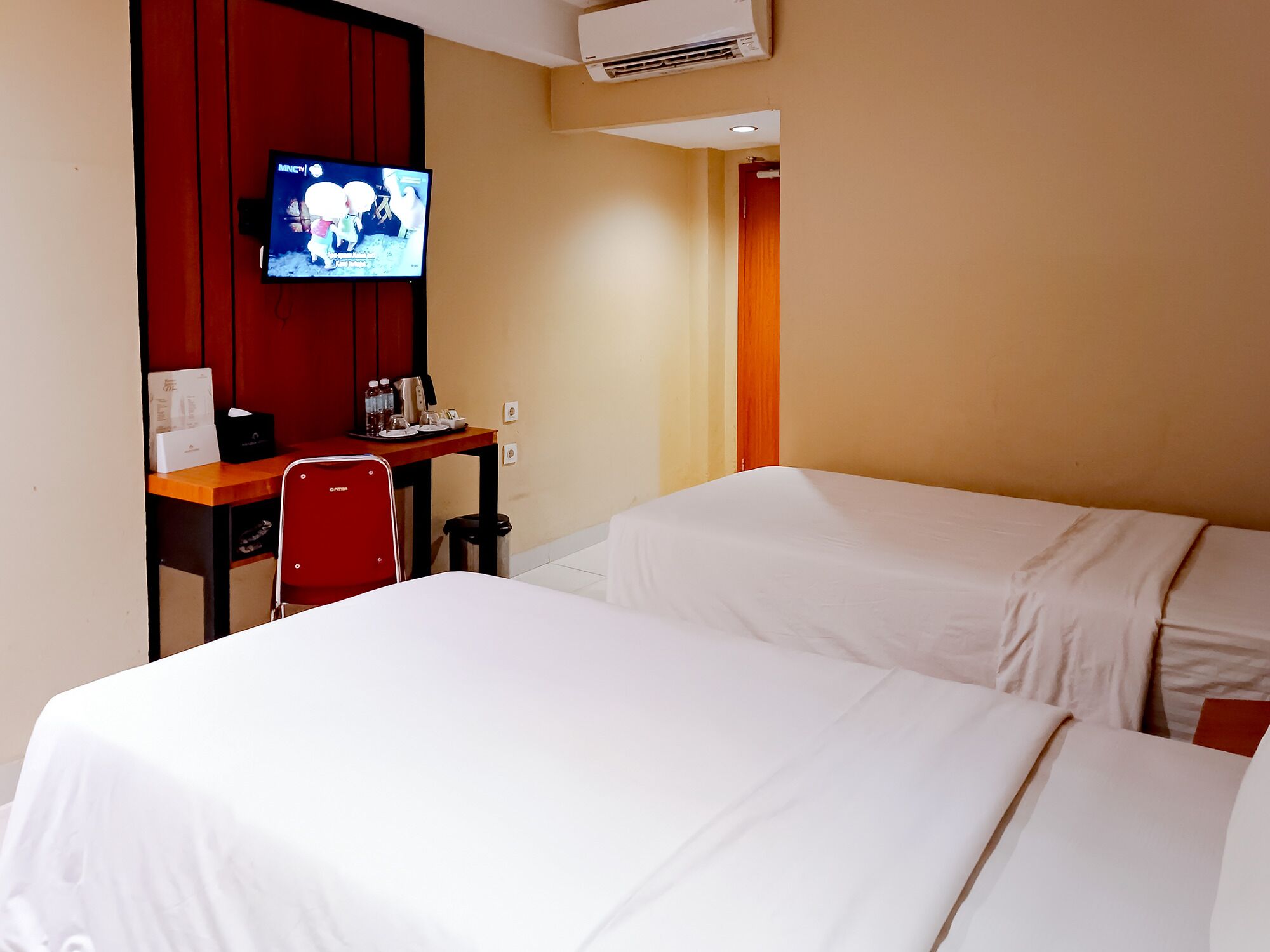 A hotel room with two beds, a desk with a chair, a television, and a small table with a coffee maker and other items.