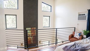 Ein modernes Schlafzimmer mit Balkon, großen Fenstern, einer dekorativen Metallwand und einem gemütlichen Sessel.