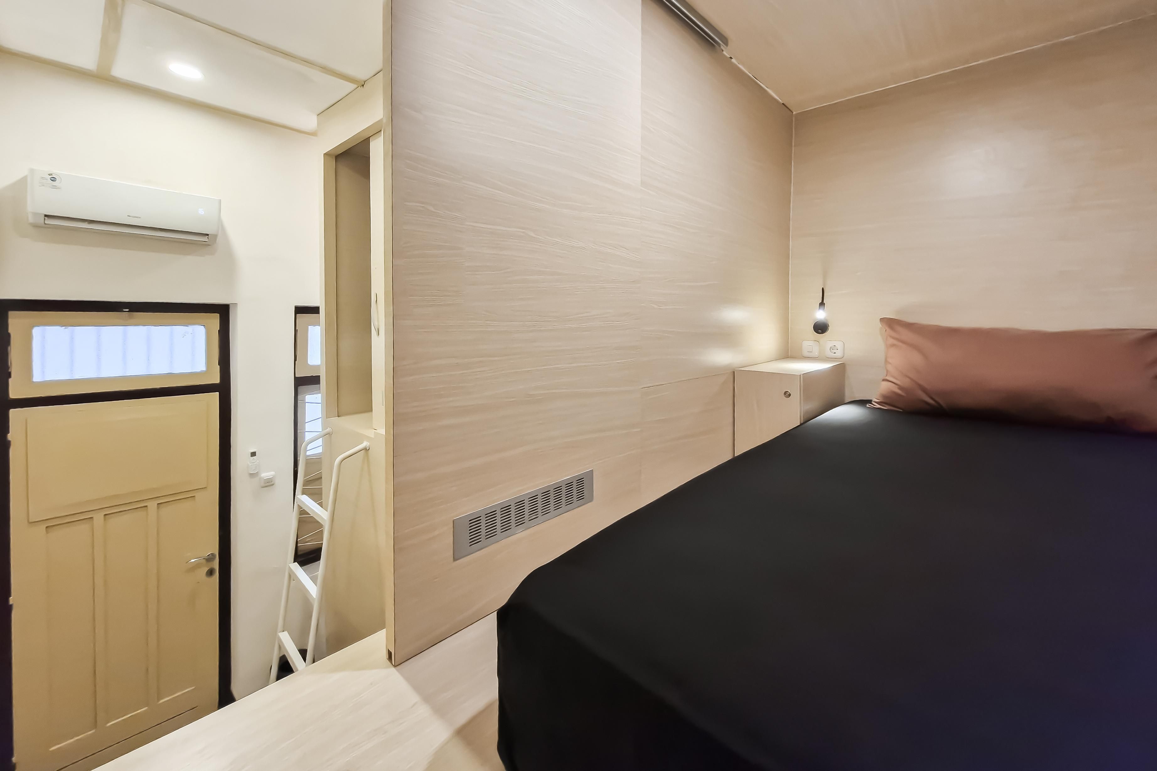 Une chambre à coucher comprenant un lit, une table de chevet, une lampe fixée au mur et une porte donnant sur une salle de bain.
