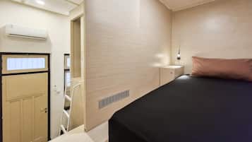 Un dormitorio con cama, mesita de noche, lámpara de pared y puerta que da al baño.