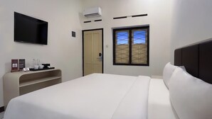 A hotel room with a bed, a TV mounted on the wall, an air conditioning unit, a window with a view, and a small shelf with a coffee maker and cups. - D'Pavilion Malioboro (Yogyakarta)