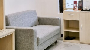 A room with a grey sofa, a wooden cabinet, a small table, and a window with a view. - D'Pavilion Malioboro (Yogyakarta)