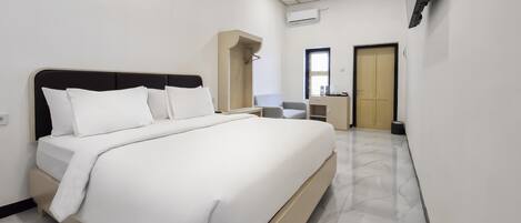 A modern hotel room with a large bed, a desk, a chair, a wardrobe, and a bathroom.