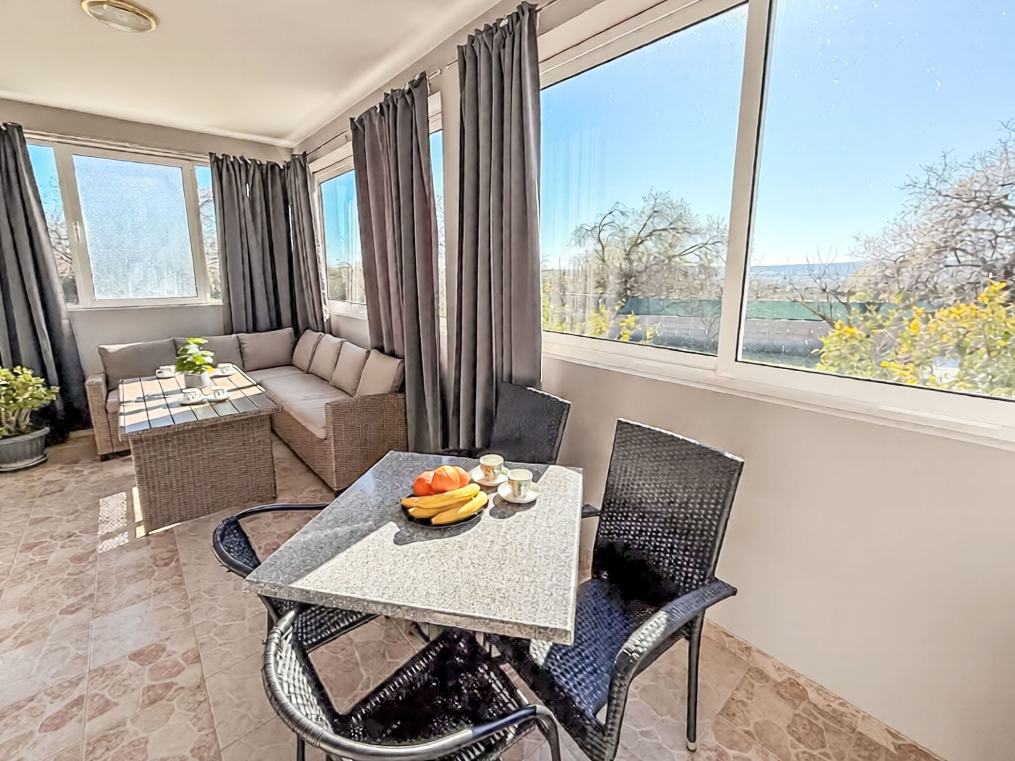 Ein sonnendurchflutetes Zimmer mit Esstisch, Stühlen, einer Couch und einem Fenster mit Vorhängen.