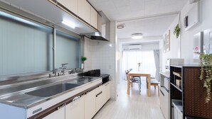 A modern kitchen with a stainless steel sink, white cabinets, and a wooden dining table with chairs. - Kamata Smile House (Tokyo)