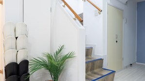 A modern interior with a staircase, a seating area with chairs, a plant, and a shoe rack. - Kamata Smile House (Tokyo)