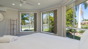 A bedroom with a large bed, a ceiling fan, and a view of a landscaped area with palm trees. - 114 Elizabeth on the Forster Keys (Forster)