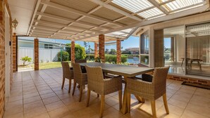 A covered patio with a dining table and chairs, brick pillars, and a view of a backyard and a body of water. - 114 Elizabeth on the Forster Keys (Forster)