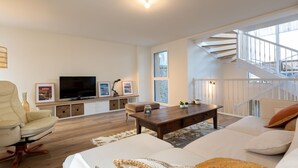 A modern living room with a sofa, a coffee table, a TV, and a staircase. - L'Oiseau 1 by Interhome (Dinard)