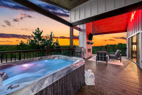 Un bain à remous sur une terrasse en bois avec vue sur le coucher de soleil, un barbecue et des sièges d’extérieur.