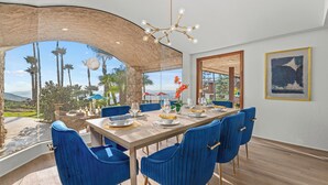 Un comedor con una mesa grande, sillas azules y vistas a palmeras y montañas.