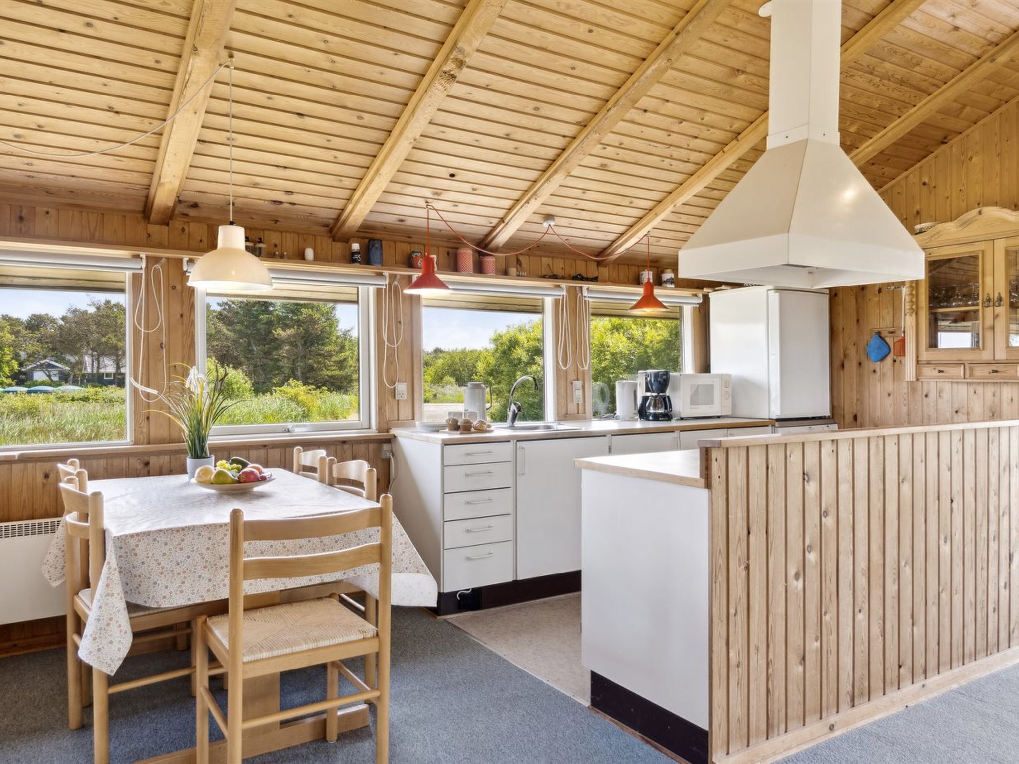 Une cabane en bois dotée d’une cuisine et d’un coin repas, avec de grandes fenêtres et une vue sur la verdure environnante.