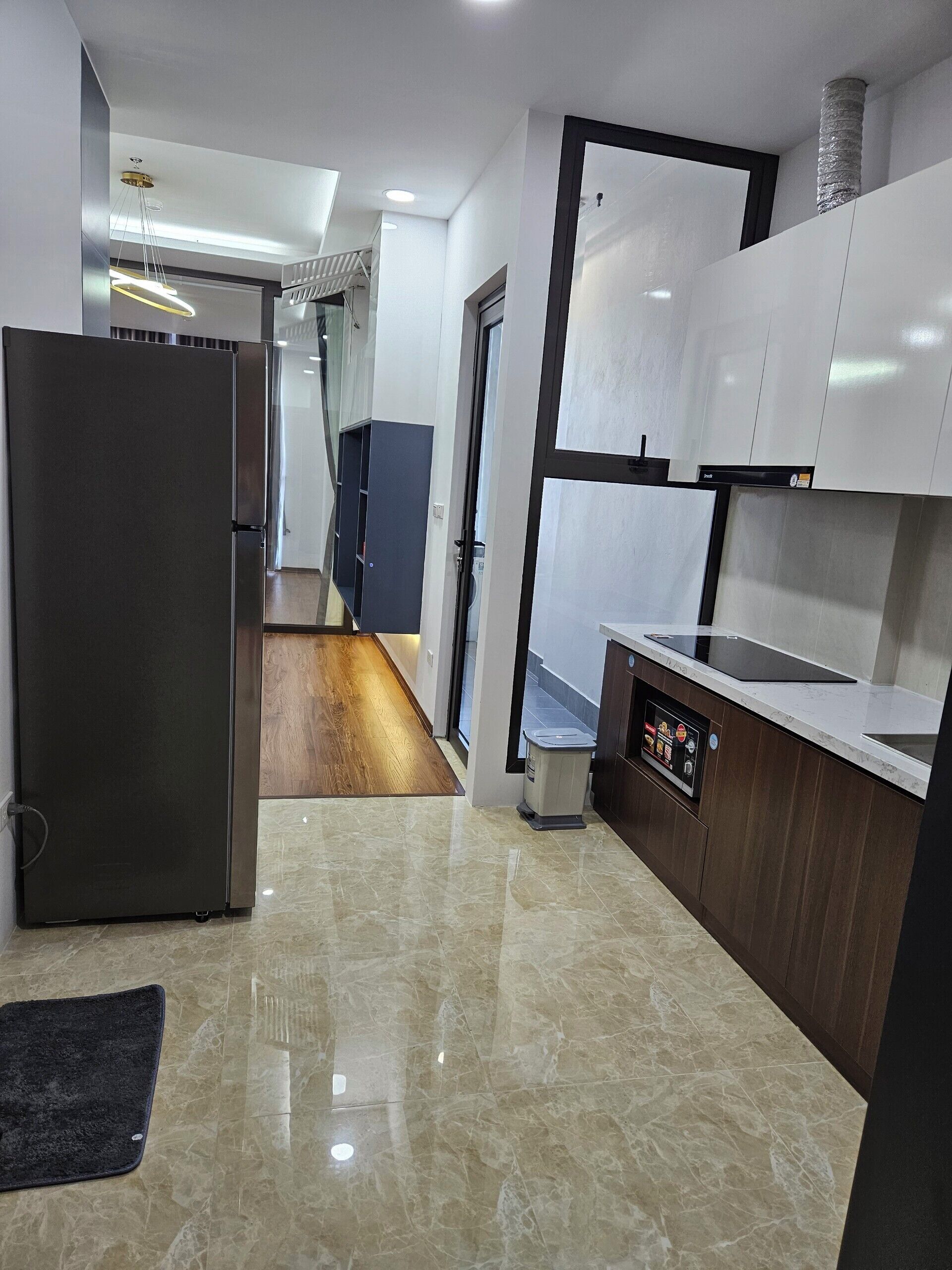 A modern kitchen with a stainless steel refrigerator, a built-in oven, and a microwave. There is a wooden floor and a marble countertop.