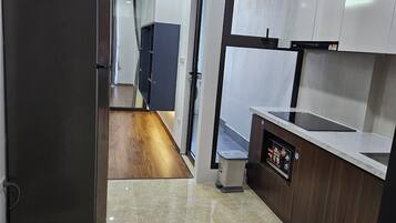 A modern kitchen with a stainless steel refrigerator, a built-in oven, and a microwave. There is a wooden floor and a marble countertop.