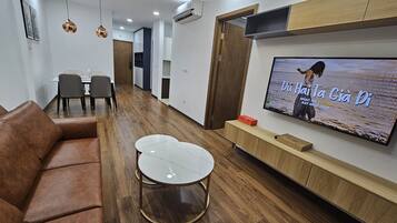 A modern living room with a brown leather sofa, a round coffee table, and a flat-screen TV mounted on the wall displaying a music video.