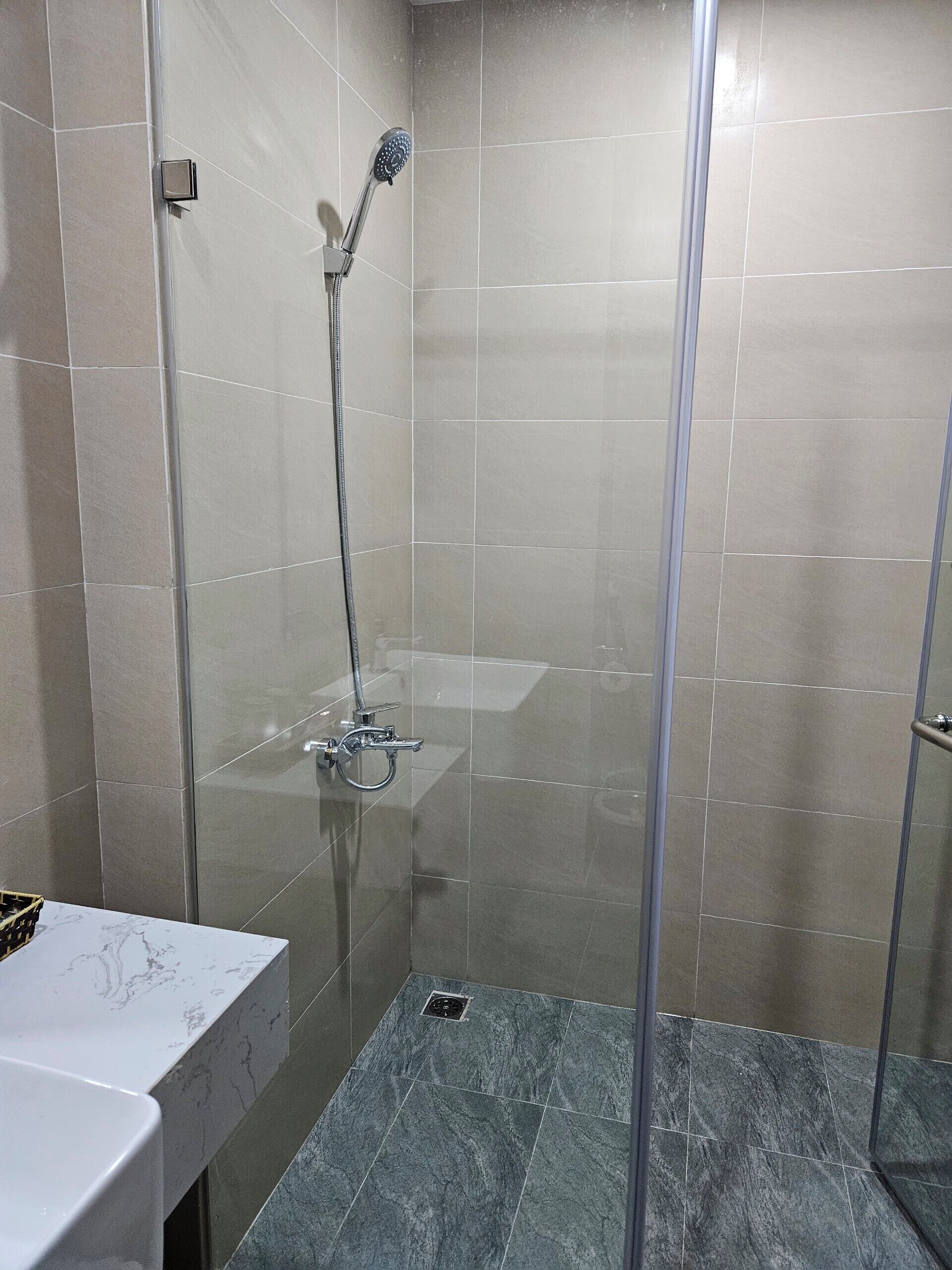 A modern bathroom with a glass-enclosed shower, a marble countertop, and a tiled floor.