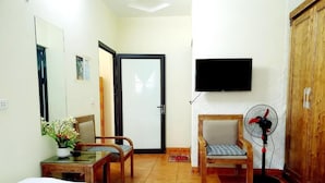 A hotel room with two beds, a desk with a plant, a chair, a wooden wardrobe, a TV, and a standing fan. - Minh Quan Sapa Hotel - by Bay Luxury (Sa Pa)