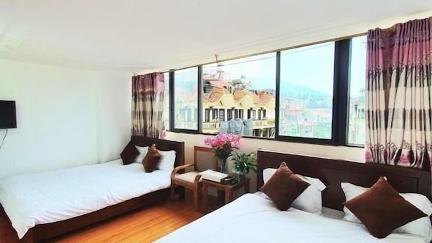 A hotel room with two single beds, a wooden floor, a small table with a vase of flowers, and large windows with curtains. - Minh Quan Sapa Hotel - by Bay Luxury (Sa Pa)
