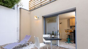 Une terrasse avec une table, deux chaises et une bouteille de vin.