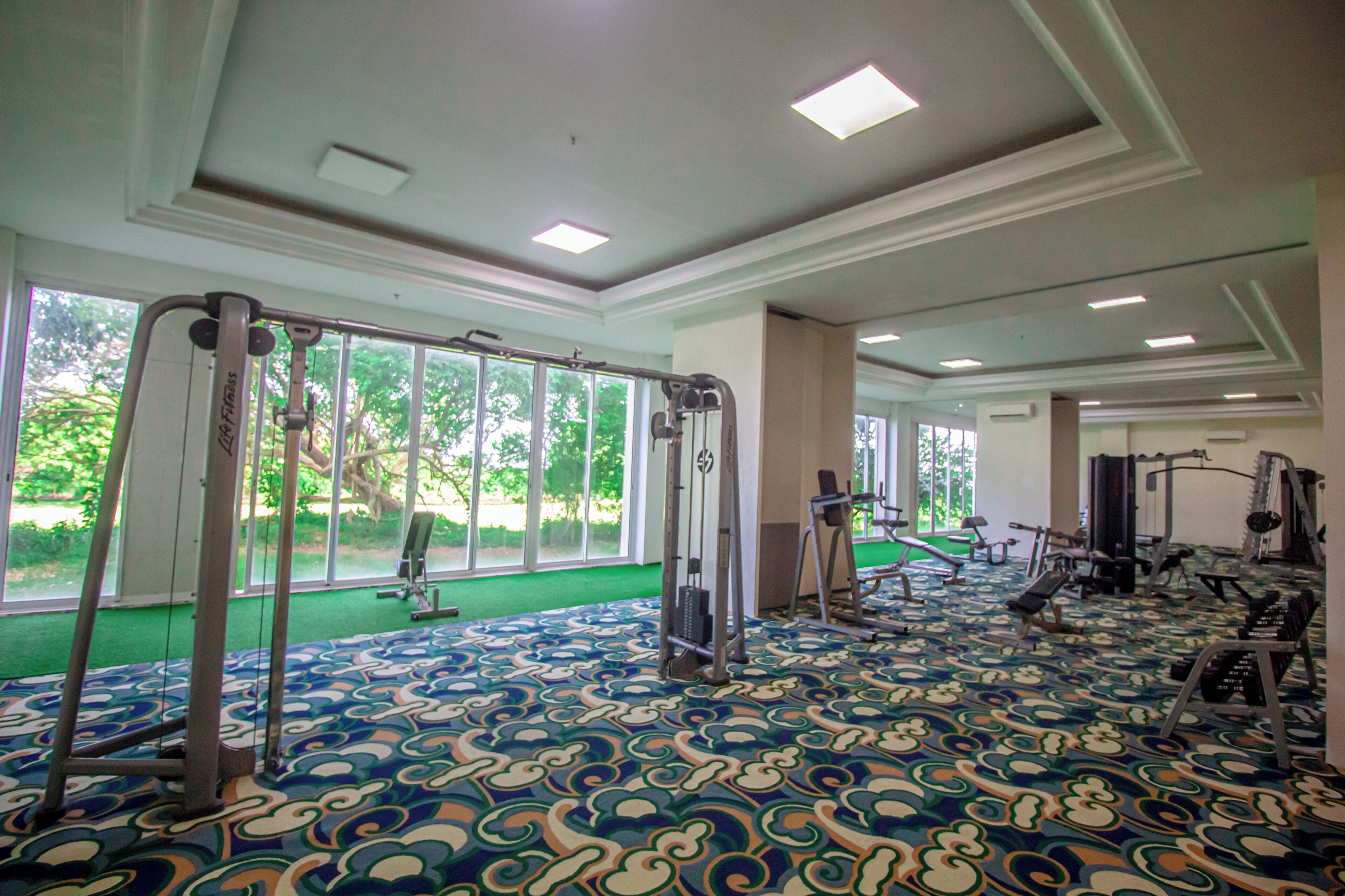 A spacious gym with large windows, exercise equipment, and a patterned carpet.