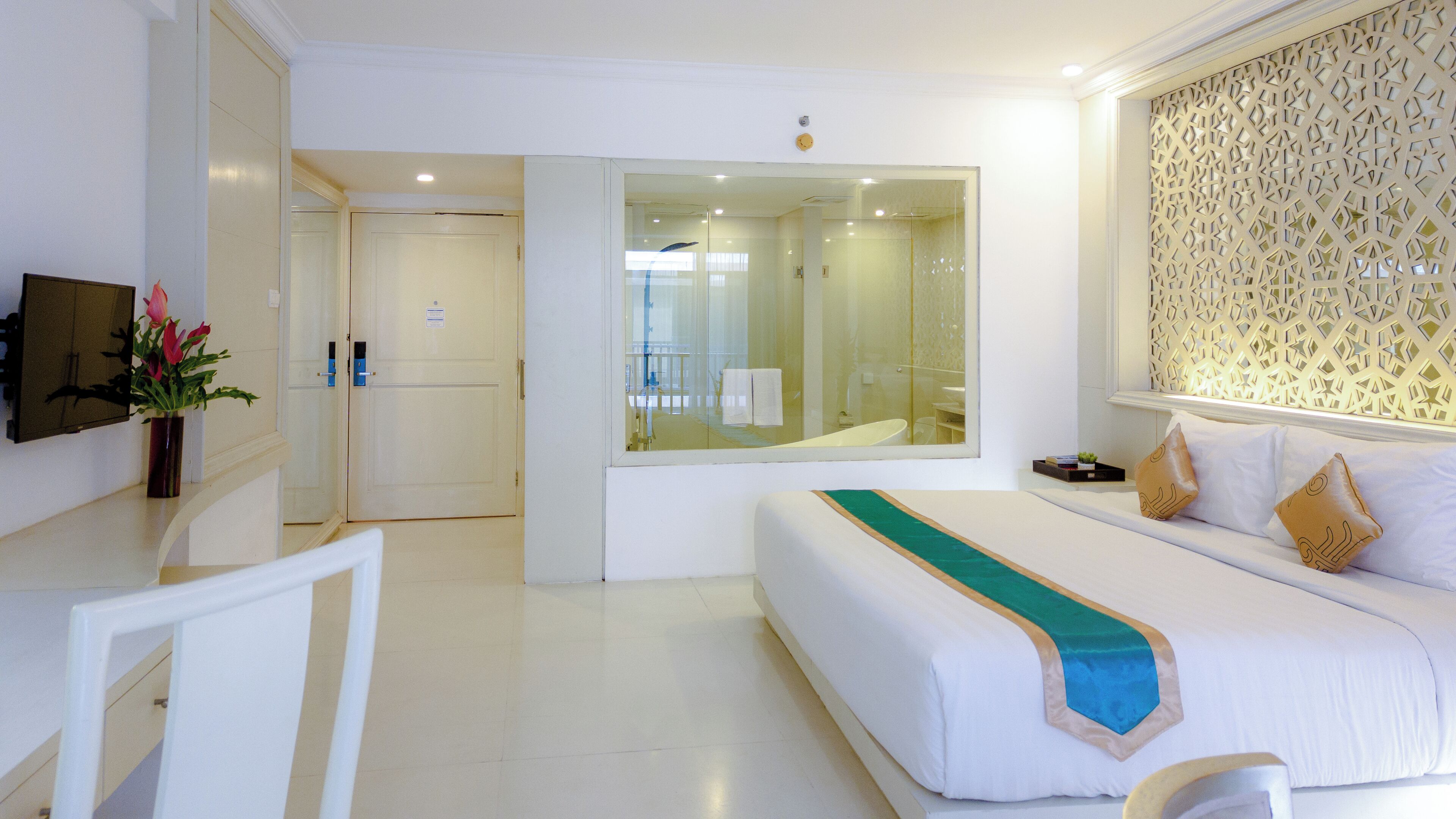 Quarto de hotel com uma cama grande, uma escrivaninha com cadeira, televisão e espelho.
