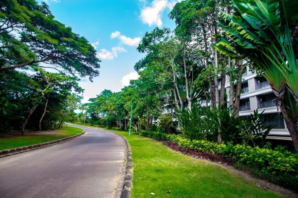 A curved road lined with lush greenery and a multi-story building with balconies.