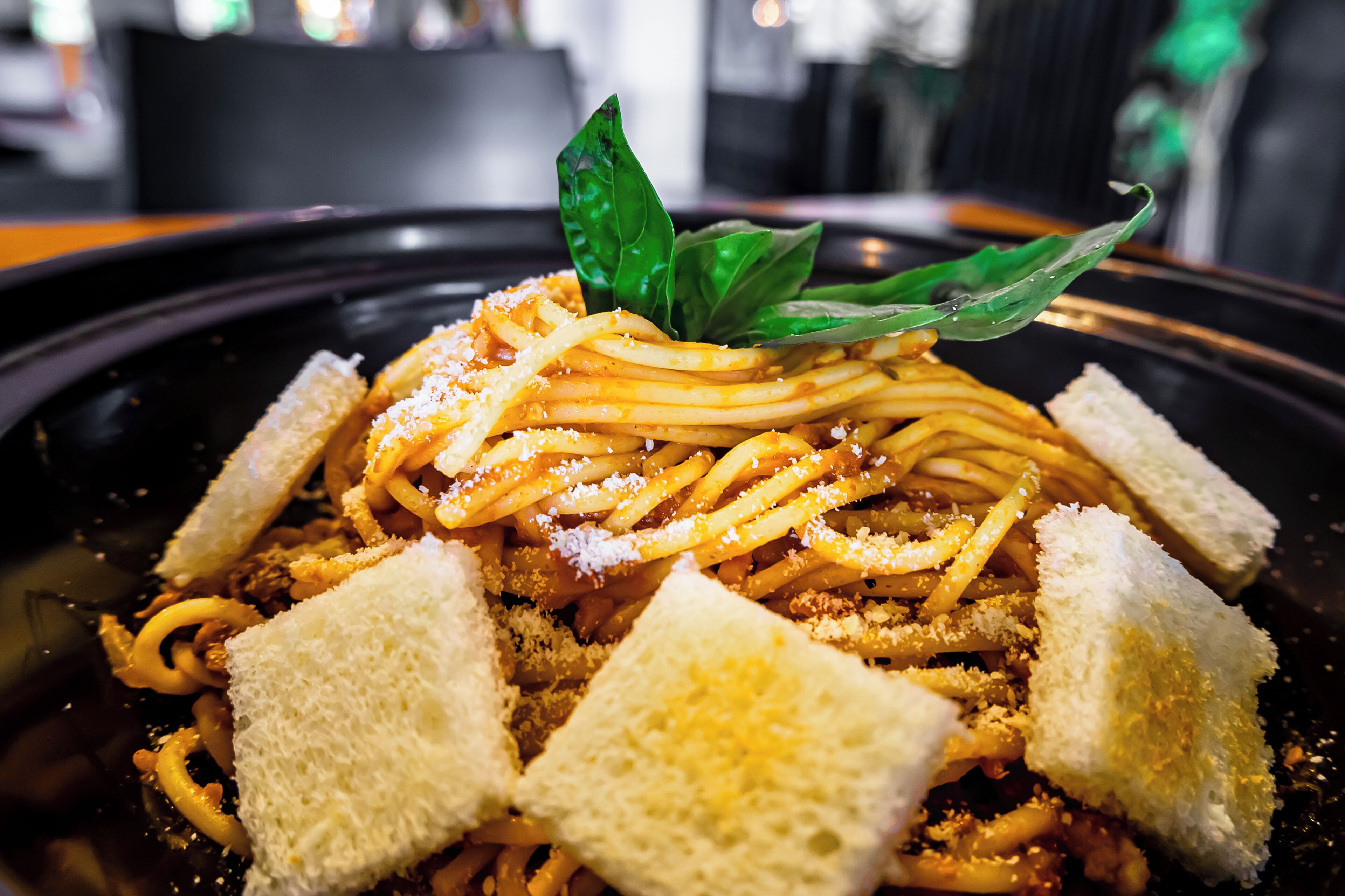 A plate of spaghetti with bread and a basil leaf garnish.
