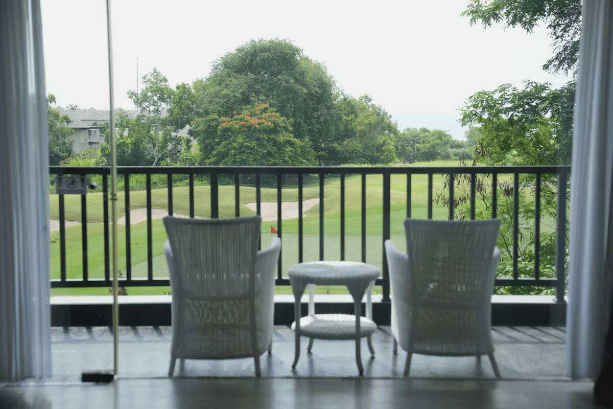 Un balcon avec des fauteuils et une table en osier, donnant sur un terrain de golf.