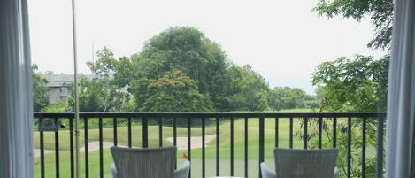 A balcony with wicker chairs and a table, overlooking a golf course.