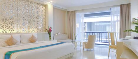 Quarto de hotel com uma cama grande, uma escrivaninha, uma cadeira e uma varanda com cortinas.