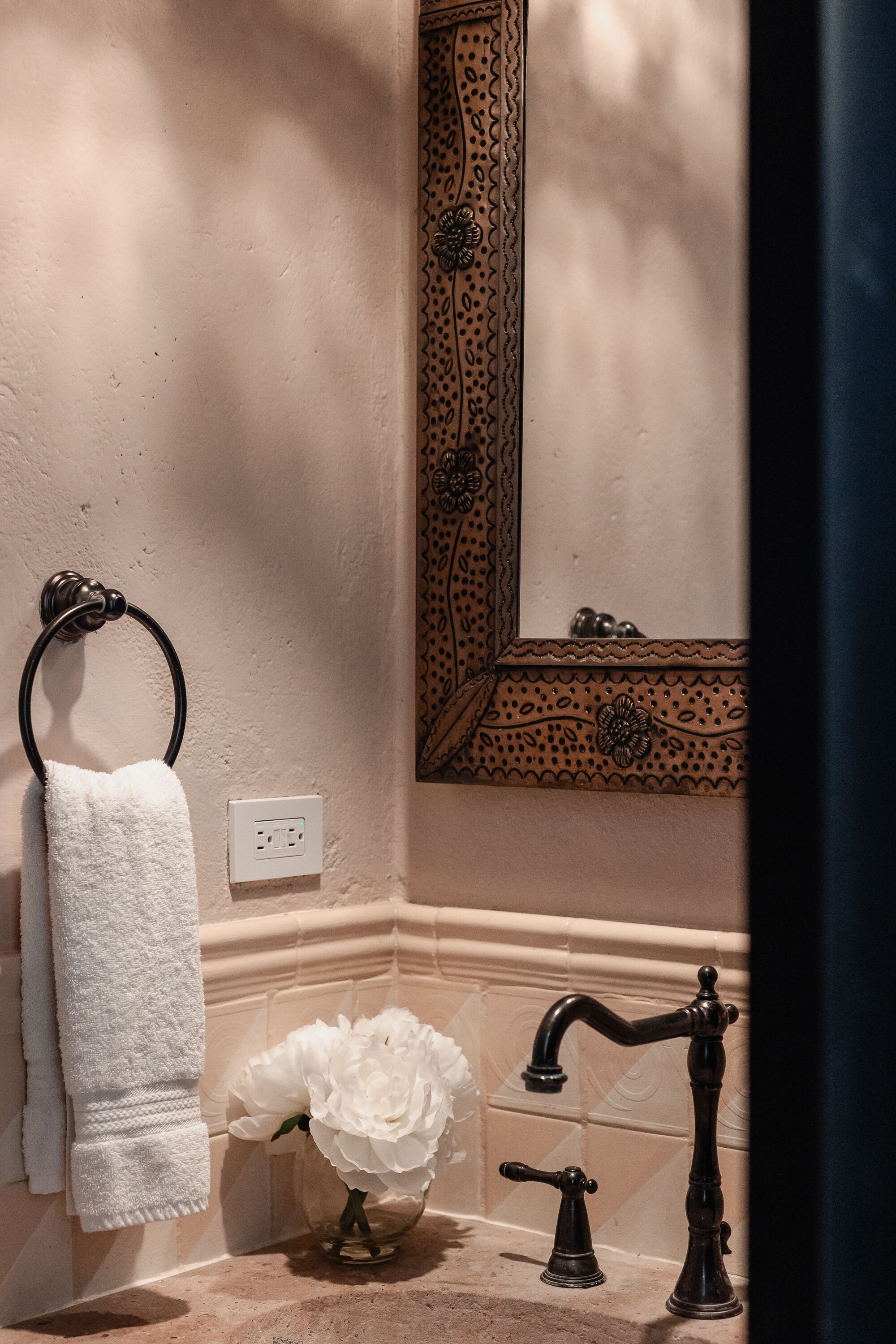 A bathroom with a towel rack, a flower vase, a mirror, and a sink with an antique faucet.