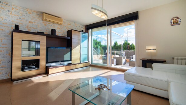 A modern living room with a glass coffee table, a flat-screen TV, a sofa, and a view of the outdoors through large sliding doors. - Casa Viena by Interhome (Albir)