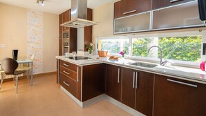 A modern kitchen with wooden cabinets, stainless steel appliances, and a window with a view of greenery. - Casa Viena by Interhome (Albir)