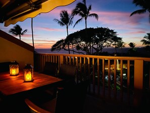 Ein Balkon mit Holellenterrassierung, ein Tisch mit zwei Laternen und Blick auf Palmen und das Meer im Abendlicht.