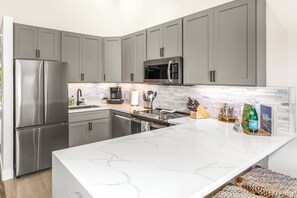 A modern kitchen with grey cabinets, stainless steel appliances, a white marble countertop, and a tiled backsplash. - Upscale & Luxurious Oceanview Resort Vistas (Kihei)