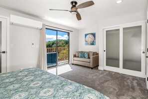 Ein Schlafzimmer mit einem Bett, einem Deckenventilator, einer Schiebetür zu einem Balkon, einem beigen Sofa und einem Bild an der Wand.