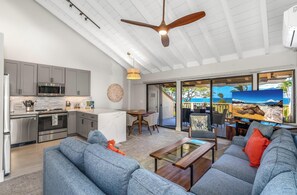 A modern kitchen with a microwave, oven, and stainless steel appliances. There is a dining area with a table and chairs, and a living room with a sofa and a coffee table. - Upscale & Luxurious Oceanview Resort Vistas (Kihei)