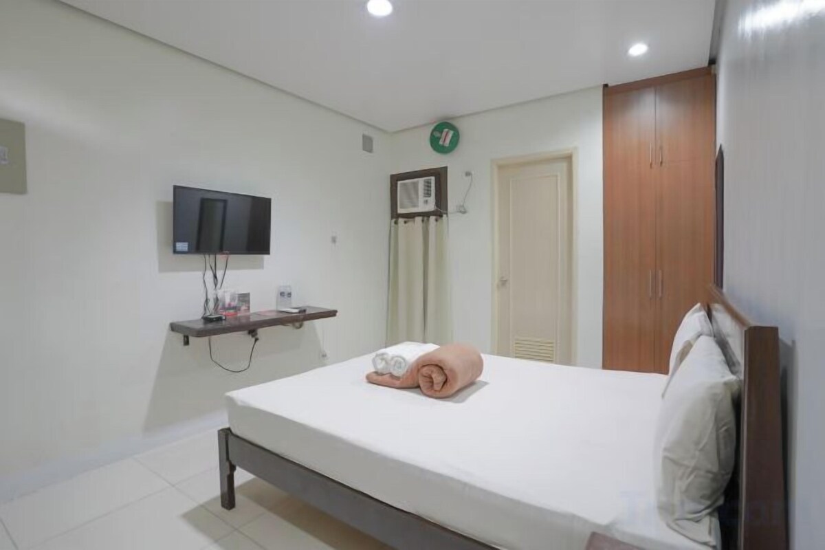 A bedroom with a bed, a television on a shelf, a wardrobe, and a door.